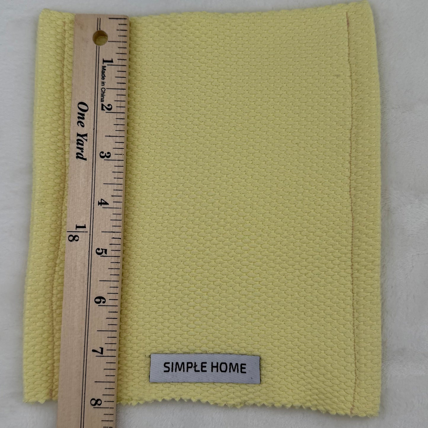 Yellow fabric swatch with a ruler and 'Simple Home' label on a gray background