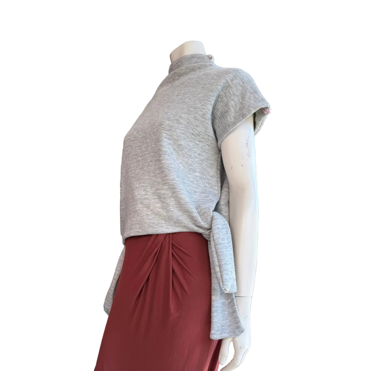 Mannequin wearing a gray top and red skirt in a room with a television displaying a woman's face.