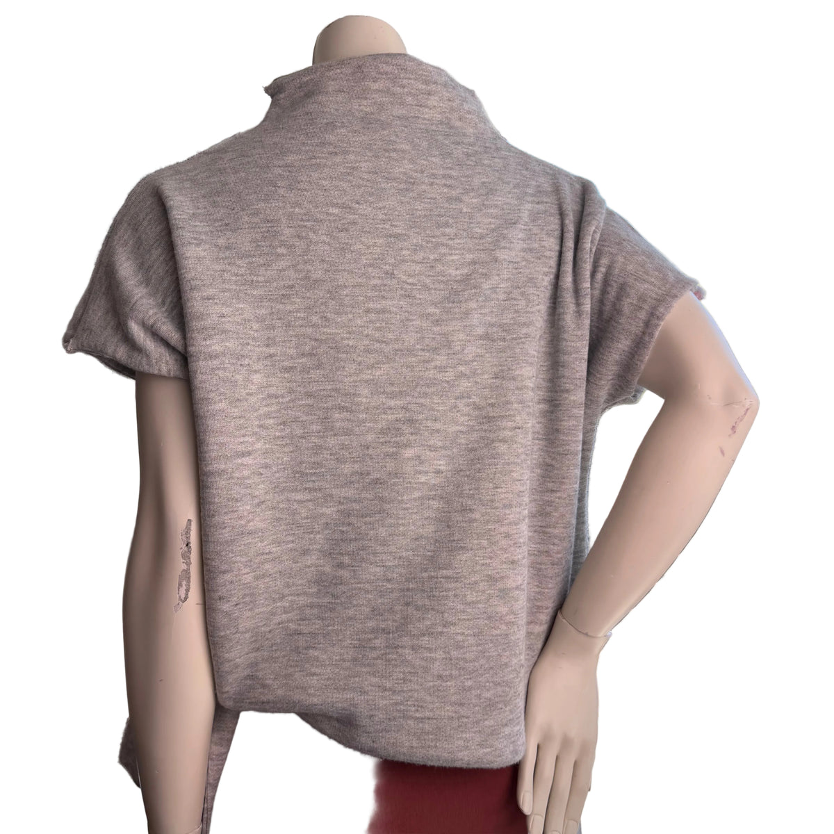 A short-sleeve knit top in a heathered taupe-gray color, shown from the back on a mannequin. The mannequin is positioned indoors near a window with a view of trees and sky, wearing a dark red skirt or pants.