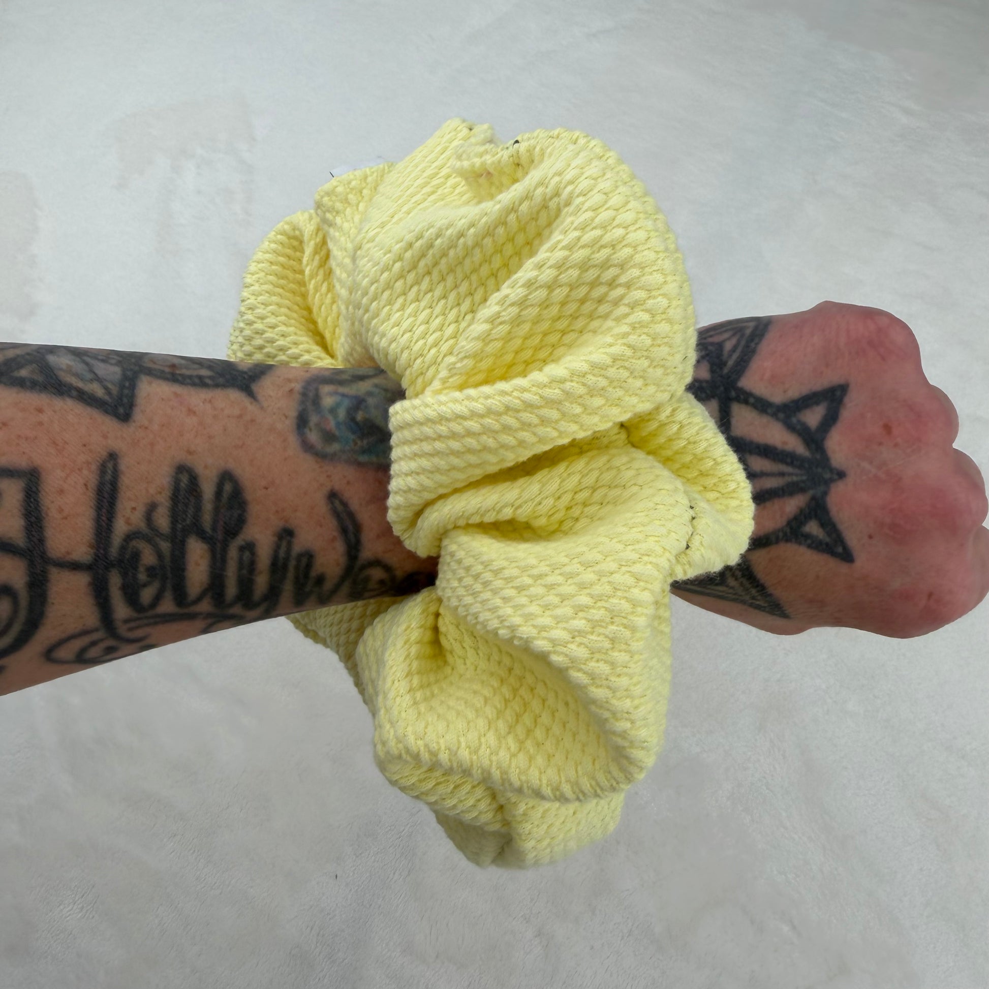 Yellow scrunchie held by a tattooed arm on a white background